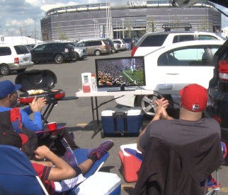 Men sitting in chairs and tailgating outside of an arena while using their unlimited antenna to watch the football game.